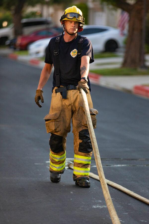 An Orange County firefighter carries a hose while responding to a burning car in Irvine, Calif., on Aug. 17, 2020. (John Fredricks/The Epoch Times)