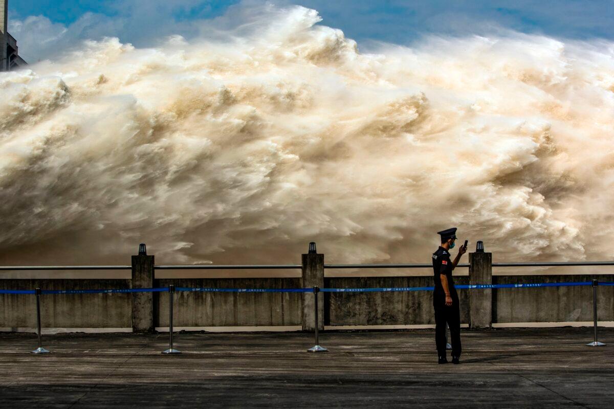 A security guard looking at his smartphone while water is released from the Three Gorges Dam, a gigantic hydropower project on the Yangtze River, to relieve flood pressure in Yichang, central China's Hubei Province, on July 19, 2020. (STR/AFP via Getty Images)