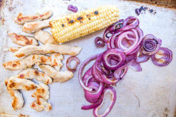 Throw seasoned chicken tenders, red onions, and corn on the cob onto the grill for a quick cook. (Caroline Chambers)