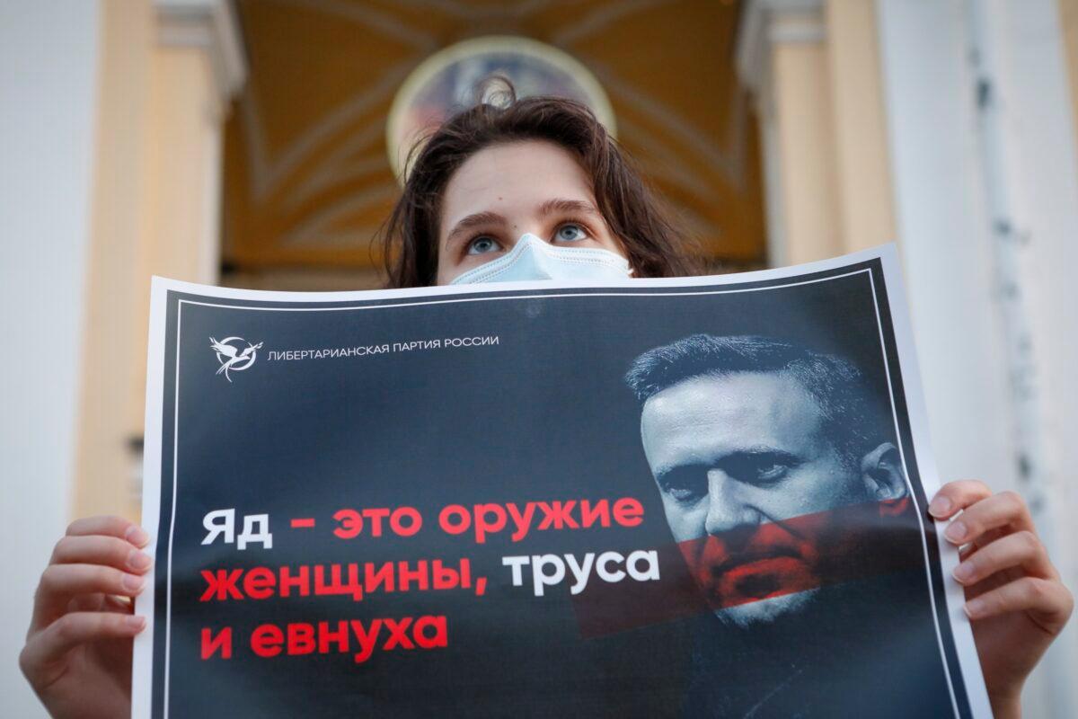 A protester stands holds a poster reads "poison is the weapon of a woman, a coward and a eunuch!" during a picket in support of Russian opposition leader Alexei Navalny in the center of St. Petersburg, Russia, on Aug. 20, 2020. (Elena Ignatyeva/AP Photo)
