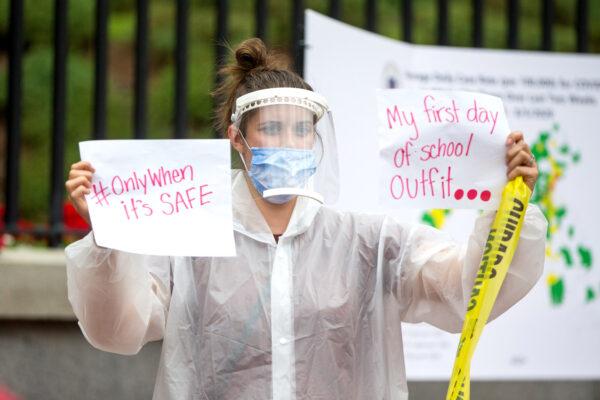 A woman in personal protective equipment holds up signs at a standout protest organized by the American Federation of Teachers at the Massachusetts State House in Boston, Mass., on Aug. 19, 2020. (Scott Eisen/Getty Images)
