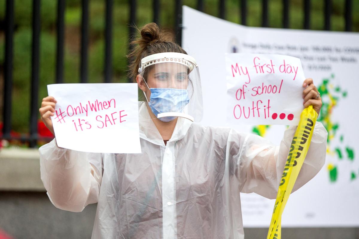 A woman in personal protective equipment holds up signs at a standout protest organized by the American Federation of Teachers at the Massachusetts State House in Boston, on Aug. 19, 2020. (Scott Eisen/Getty Images)