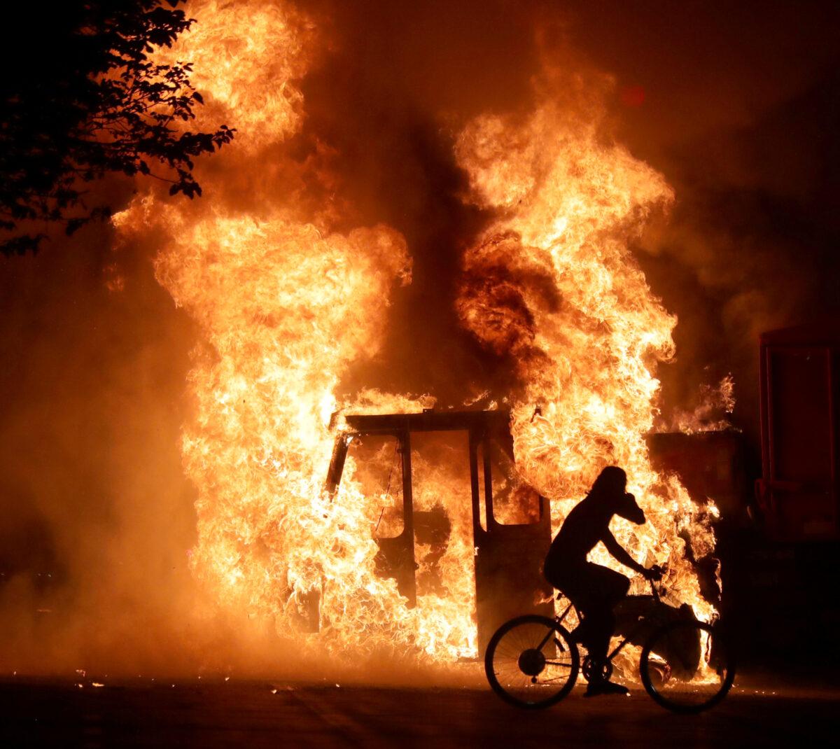 A man on a bike rides past a city truck on fire outside the Kenosha County Courthouse during riots following the police shooting of Jacob Blake in Kenosha, Wis., on Aug. 23, 2020. (Mike De Sisti/Milwaukee Journal Sentinel via USA TODAY via Reuters)
