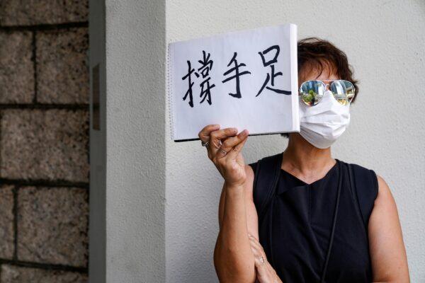 A woman holds up a paper pad that reads "support sibling" while waiting outside the court to bid farewell to a prison van transporting Tong Ying-kit, a Hong Kong resident charged under the city's new national security law, on Aug. 25, 2020. (Lam Yik via Reuters)