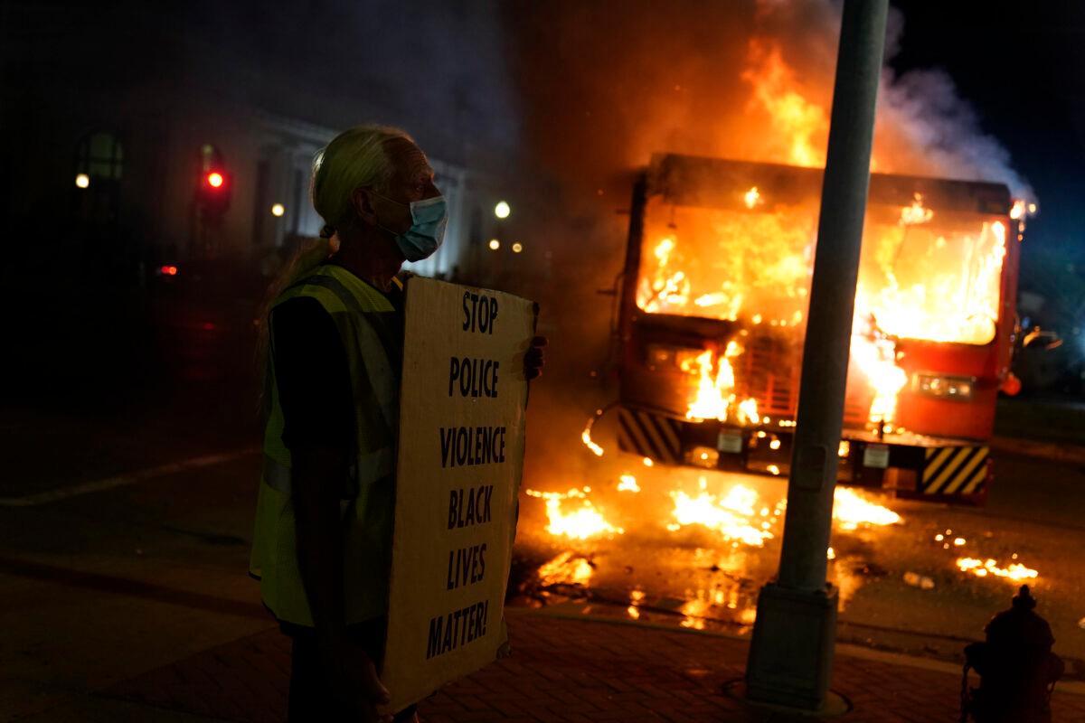 A man stands with a "Black Lives Matter" sign near a burning garbage truck in Kenosha, Wis., on Aug. 24, 2020. (Morry Gash/AP Photo)