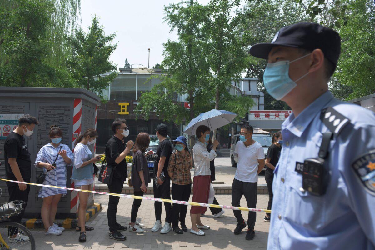 A policeman keeps watch as people wait in line to undergo COVID-19 swab tests at a testing station in Beijing on June 28, 2020. (Greg Baker/AFP via Getty Images)