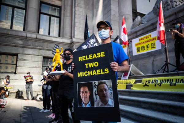 A man holds a sign with photographs of Michael Kovrig and Michael Spavor, who have been detained in China since December 2018, as people gather for a rally in support of Hong Kong democracy, in Vancouver on Aug. 16, 2020. (The Canadian Press/Darryl Dyck