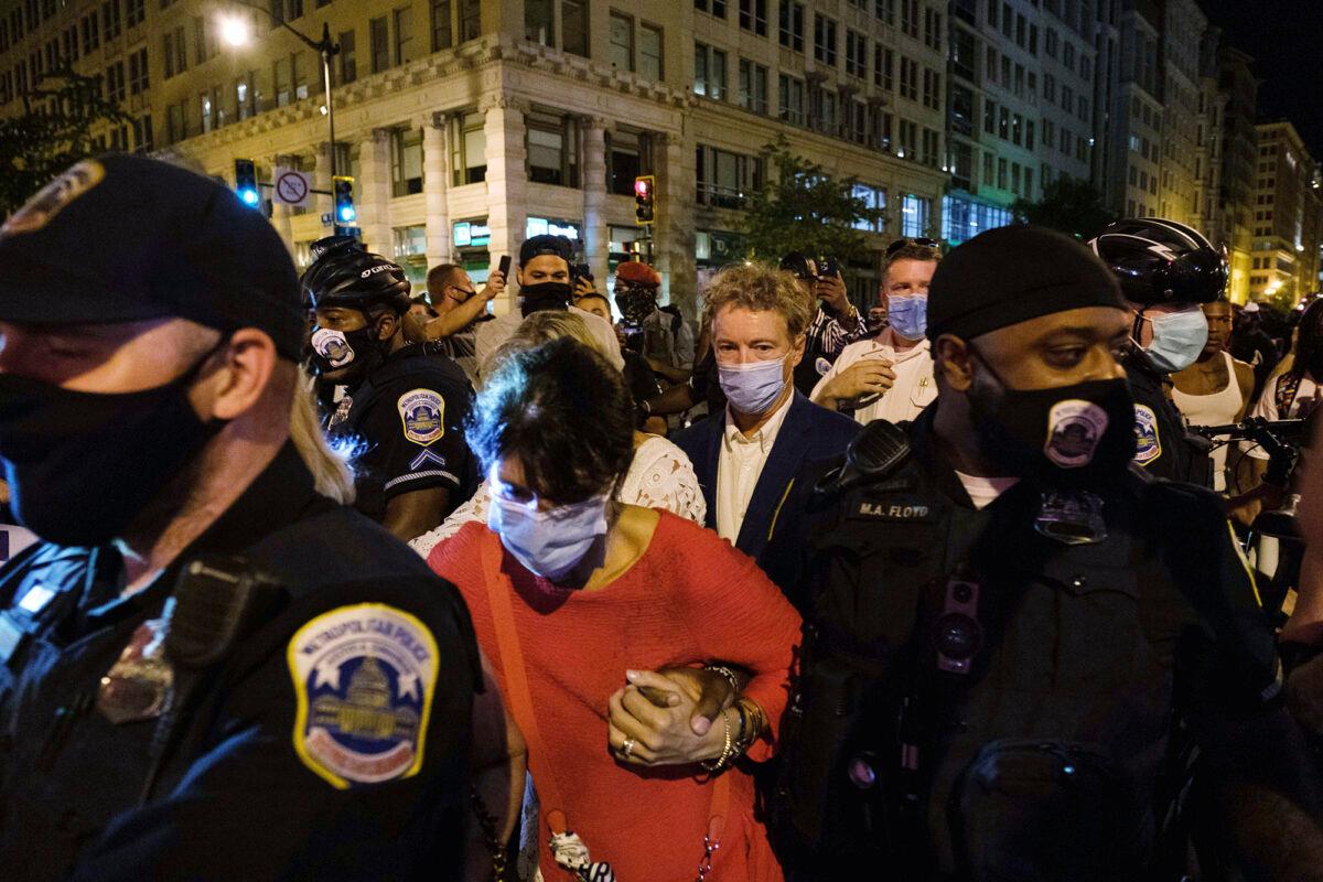  Sen. Rand Paul (R-Ky.) (C) and three women are escorted by police officers through a crowd in Washington on Aug. 28, 2020. (Yuki Iwamura/AP Photo)