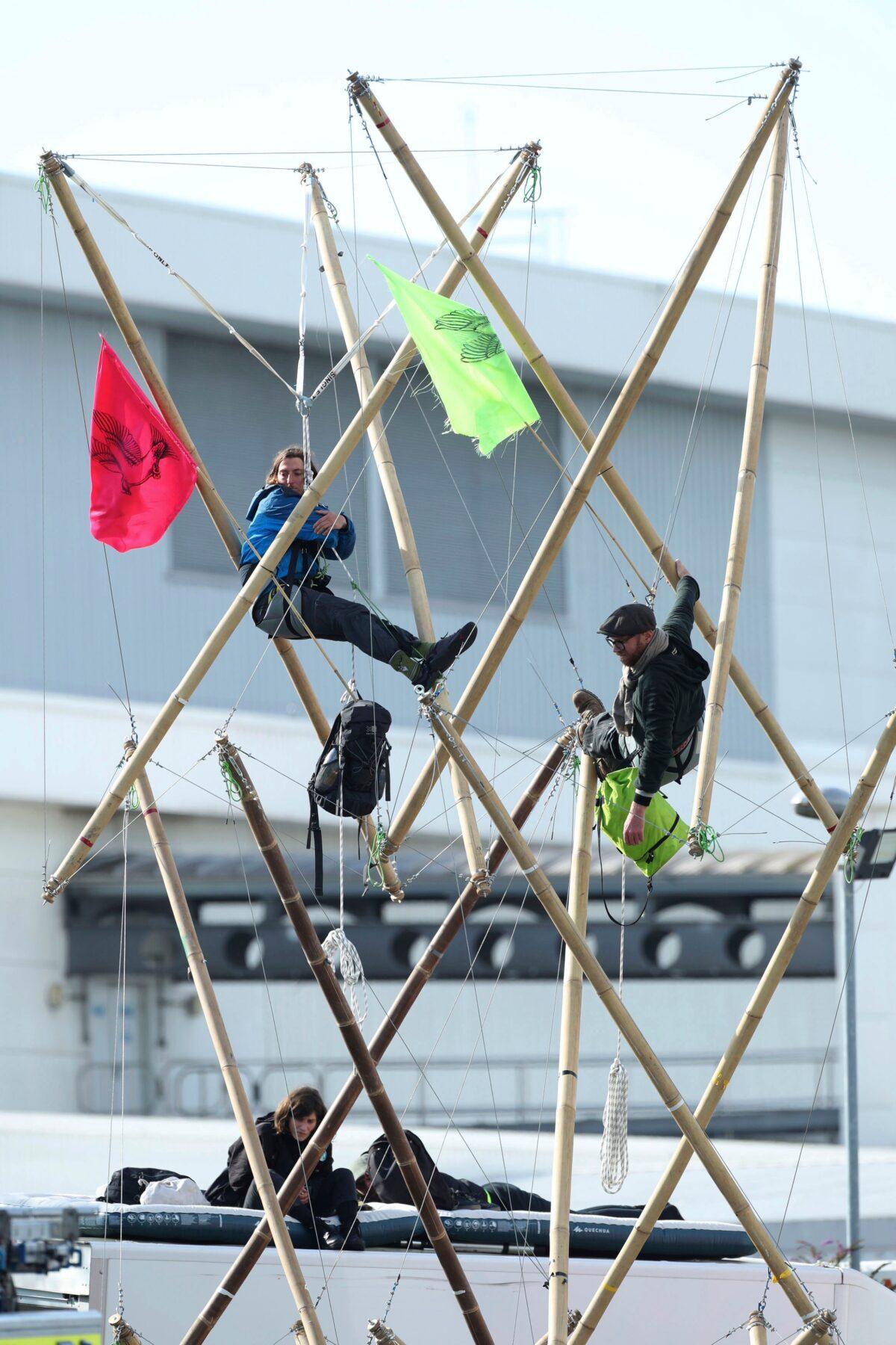 Two protesters attached to bamboo and two sitting on the roof of a van block the road, outside Broxbourne newsprinters in Hertfordshire, England, on Sept. 5, 2020. (Yui Mok/PA via AP)