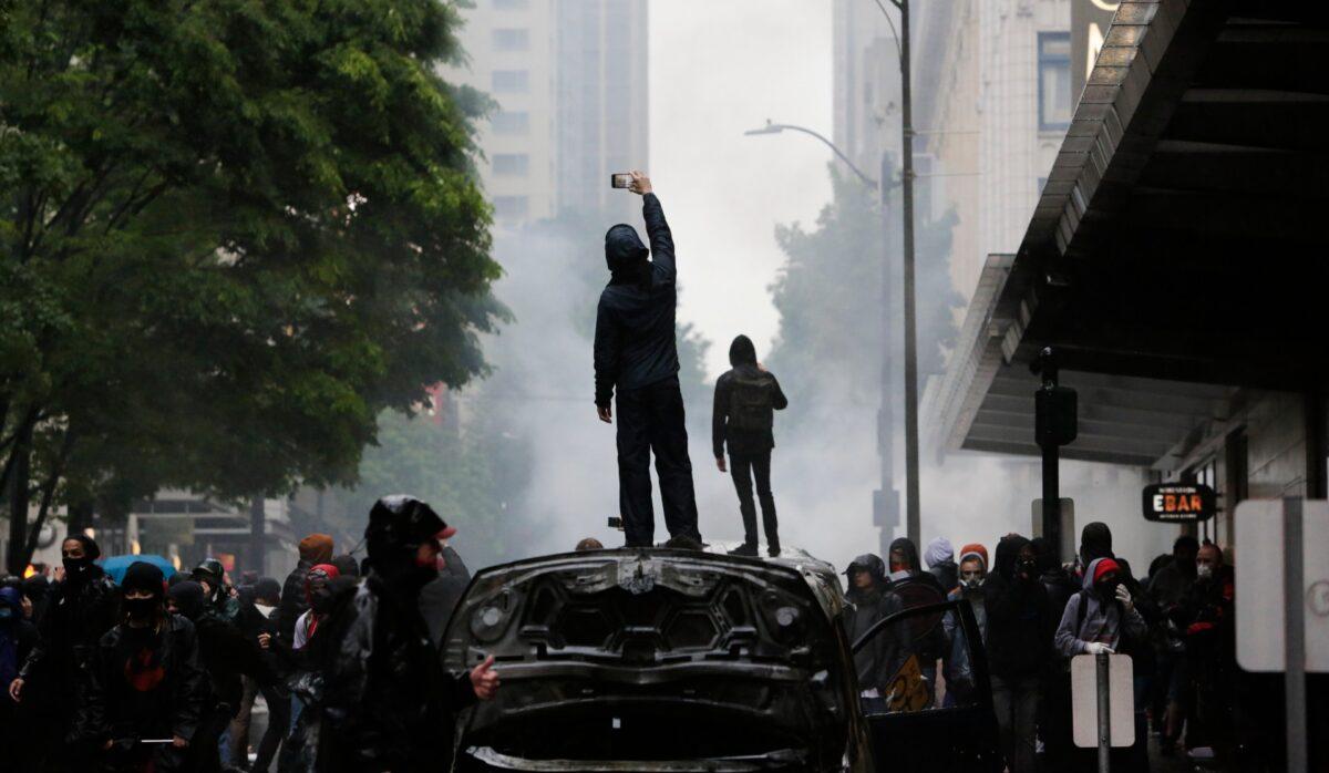 People stand on burned vehicles following demonstrations protesting in Seattle, Washington on May 30, 2020. (Photo by Jason Remond/AFP via Getty Images)