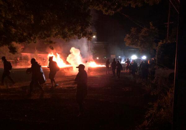 A fire lit by rioters in a street in Portland, Ore., is seen at left, as rioters move away from police, late Sept. 5, 2020. (Andrew Selsky/AP Photo)