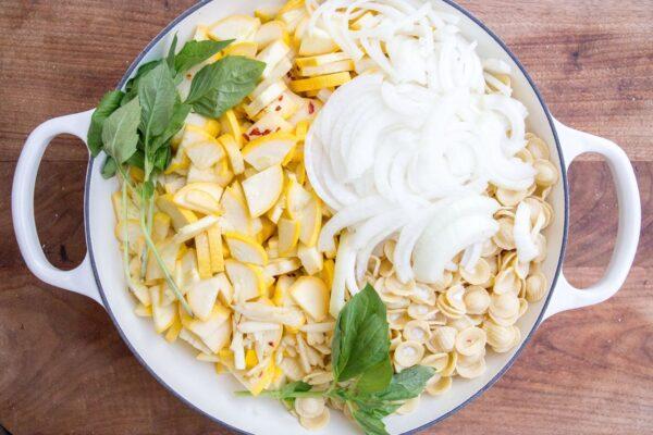 Throw your dried pasta, sliced yellow squash and onions, seasonings, and chicken broth all together in one pot on the stovetop. (Caroline Chambers)
