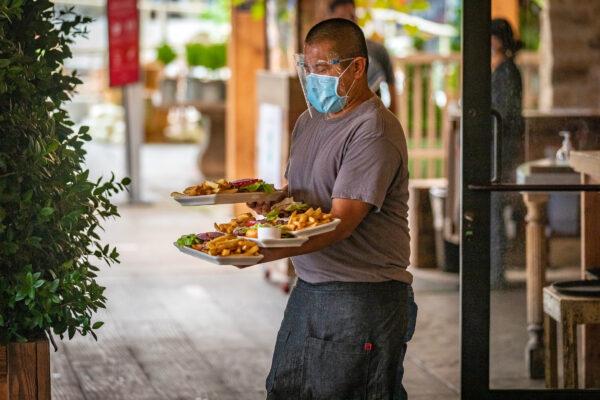 A waiter wearing protective face gear balances plates of food on his arms as he carries them to diners at Farmhouse restaurant in Newport Beach, Calif., on Sept. 9, 2020. (John Fredricks/The Epoch Times)