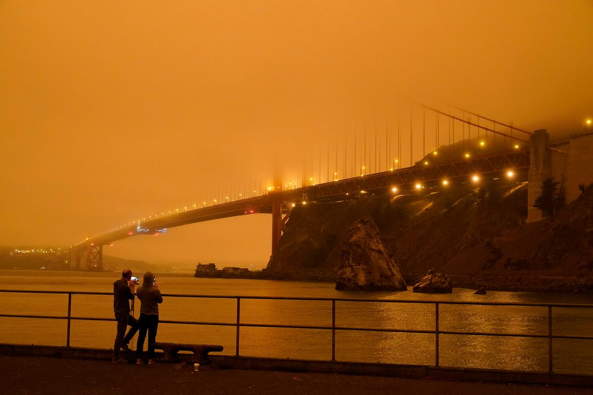 Patrick Kenefick and Dana Williams, both of Mill Valley, Calif., record the darkened Golden Gate Bridge at 9:47 a.m. covered with smoke from wildfires Wednesday, Sept. 9, 2020, from a pier at Fort Baker near Sausalito, Calif. (Eric Risberg/AP)