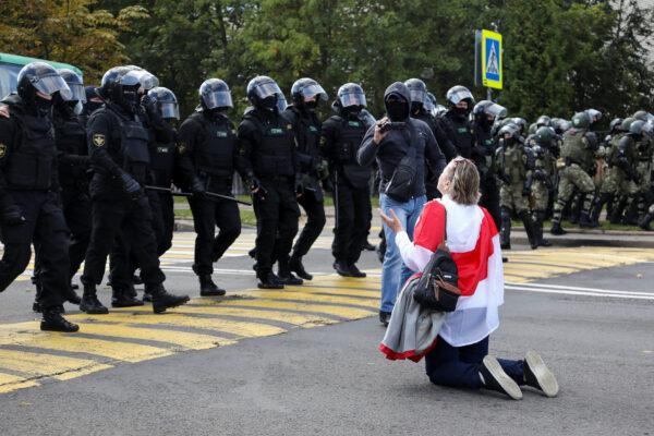 A protester with a historical white-red-white flag of Belarus kneels in front of law enforcement officers during a rally against police brutality in Minsk, on Sept. 13, 2020. (Tut.By/Reuters)