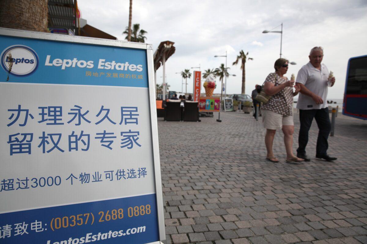 Tourists walk past a real estate promotion billboard in Chinese, which states that buying an apartment can earn permanent resident status, on the seafront promenade in the Cypriot resort of Paphos on Jan. 24, 2013. (Yiannis Kourtoglou/AFP via Getty Images)