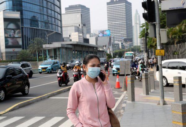 A woman wearing a mask as a precaution against the new coronavirus outbreak talks on her mobile phone on the sidewalk of a street at the main business district in Jakarta, Indonesia, on Sept. 14, 2020. (Tatan Syuflana/AP Photo)triction
