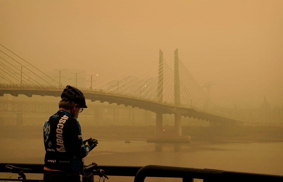 A man stops on his bike along the Willamette River as smoke from wildfires partially obscures the Tilikum Crossing Bridge, in Portland, Ore., on Sept. 12, 2020. (John Locher/AP Photo)
