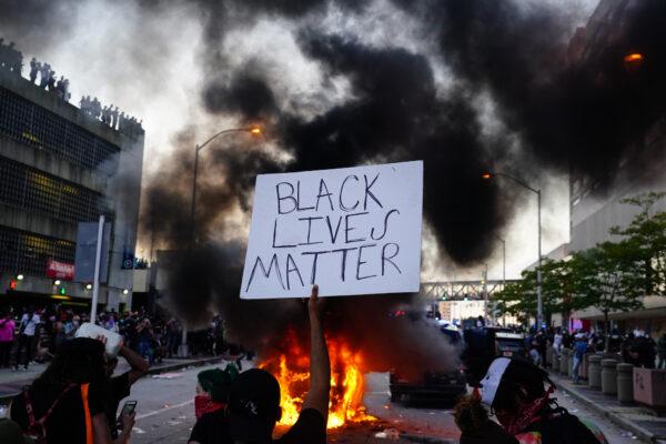 A man holds a Black Lives Matter sign as a police car burns in front of him during a protest outside CNN Center in Atlanta, Georgia, on May 29, 2020. (Elijah Nouvelage/Getty Images)