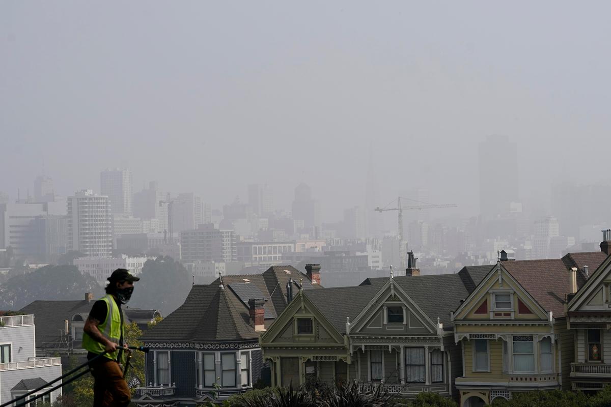 A worker waters grass at Alamo Square Park as smoke from wildfires and fog obscures the skyline above the "Painted Ladies," a row of historical Victorian homes, in San Francisco, Monday, Sept. 14, 2020. (Jeff Chiu/AP Photo)