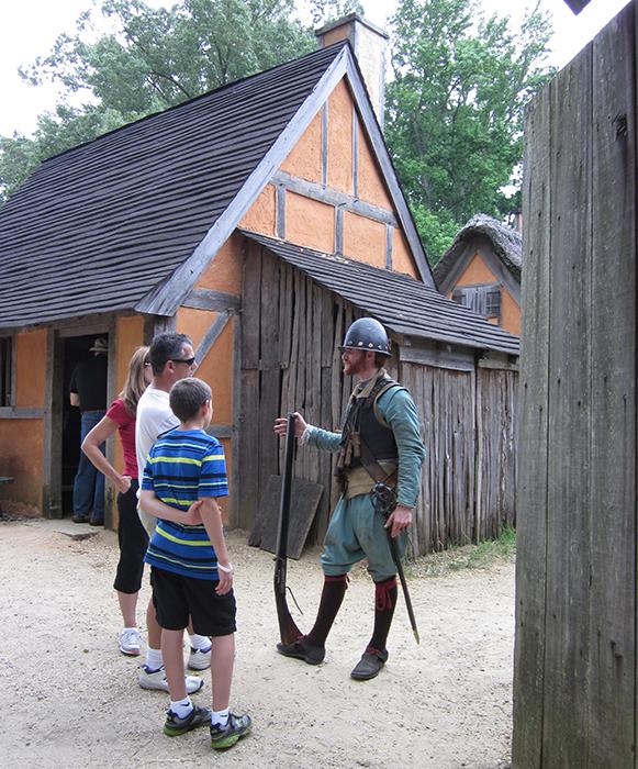 Visitors inside the triangular wooden palisade of the re-created 1610–14 James Fort, at Jamestown Settlement. The re-creation showcases wattle-and-daub structures topped with thatched roofs. (Jamestown-Yorktown Foundation)