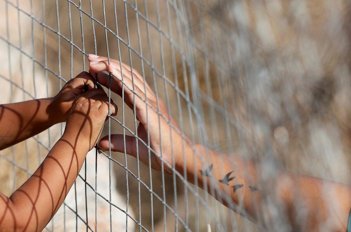 A woman touches the hands of a child through a fence at a new temporary camp for migrants and refugees, on the island of Lesbos, Greece, on Sept. 22, 2020. (Yara Nardi/Reuters)