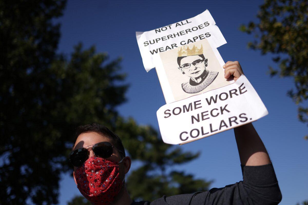 A mourner holding a sign that reads "Not all superheroes wear capes, some wore neck collars" stands outside of the U.S. Supreme Court where Associate Justice Ruth Bader Ginsburg is lying in repose, in Washington on Sept. 23, 2020. Win McNamee/Getty Images)