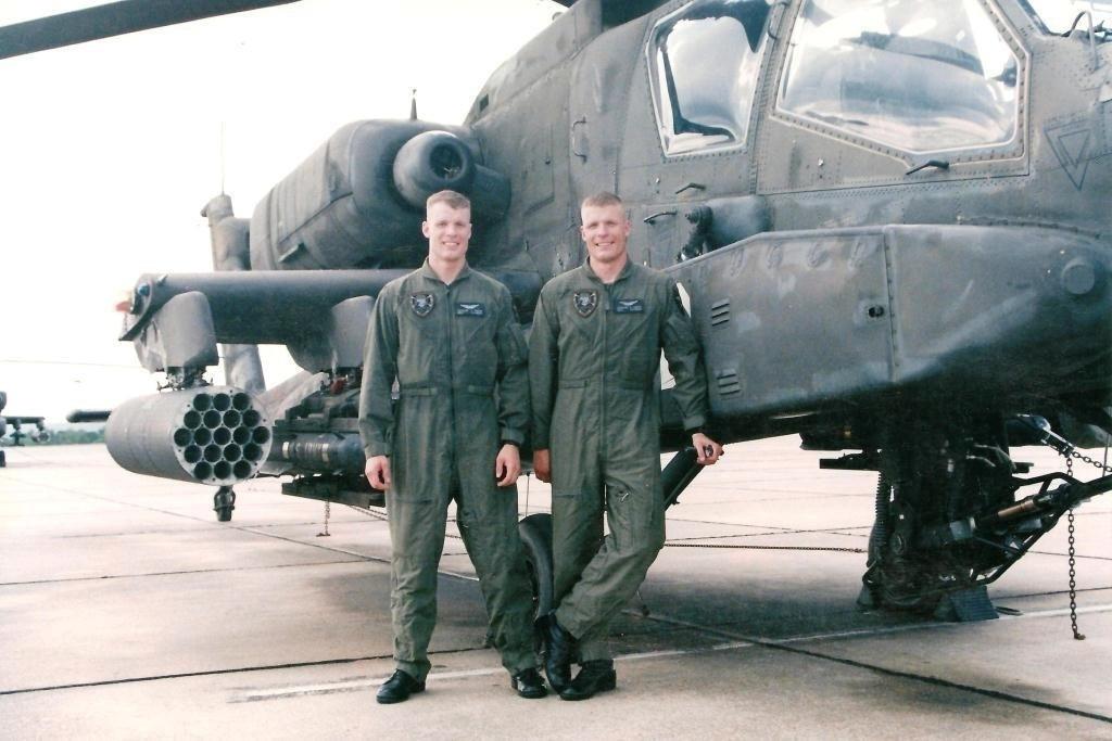 Chief Warrant Officer 4 Isaac Smith (L) and Chief Warrant Officer 4 Stewart Smith (R) pose next to an APH-64 Apache helicopter in 2003 (<a href="https://www.dvidshub.net/image/6360266/birds-feather-twin-pilots-get-apache-flight-together">CW4 Isaac and Stewart Smith</a>/DVIDSHUB)