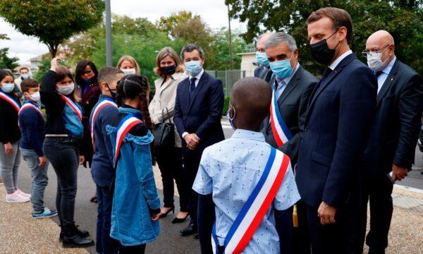 French President Emmanuel Macron, right, wearing a protective face mask speaks to youngsters standing in line outside the 'la Maison des habitants' (MDH) in Les Mureaux, northwest of Paris, on Oct. 2, 2020. (Ludovic Marin/Pool via AP)