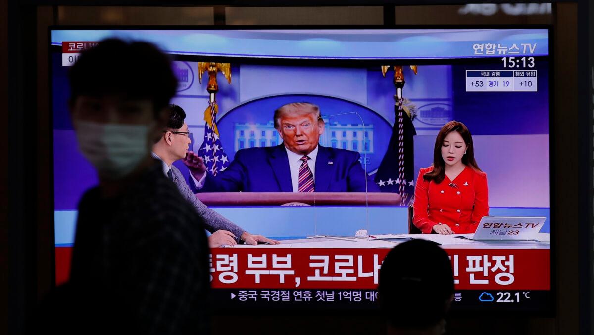 A man wearing a face mask walks near a TV screen reporting about U.S. President Donald Trump and first lady Melania Trump during a news program with a file image of Trump at the Seoul Railway Station in Seoul, South Korea, Oct. 2, 2020. (Lee Jin-man/AP Photo)