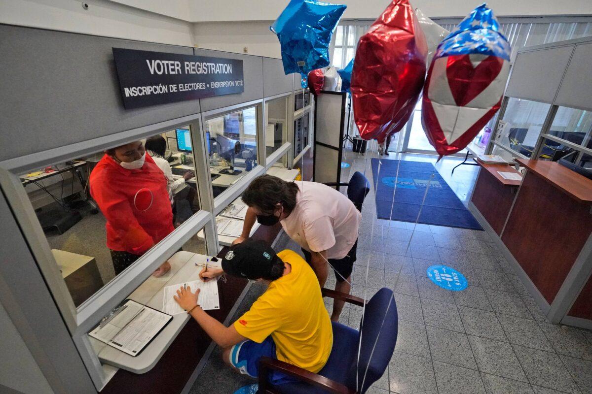 22-year-old Lucas Saez (foreground) fills out his voter registration form as his father Ramiro Saez (center rear) looks on, at the Miami-Dade County Elections Department in Doral, Fla., on Oct. 6, 2020. (Wilfredo Lee/AP Photo)