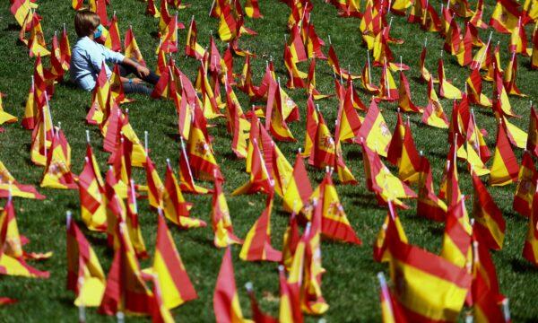 A person sits next to Spanish flags set up in memory of the coronavirus disease (COVID-19) victims in a park, in Madrid, on Sept. 27, 2020. (Sergio Perez/Reuters)