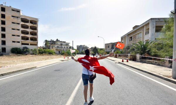 A woman walks while holding Turkish and Turkish Cypriot flags inside an area fenced off by the Turkish military since 1974, in the abandoned coastal area of Varosha, a suburb of the town of Famagusta in Turkish-controlled northern Cyprus, on Oct. 8, 2020. (Harun Ucar/Reuters)