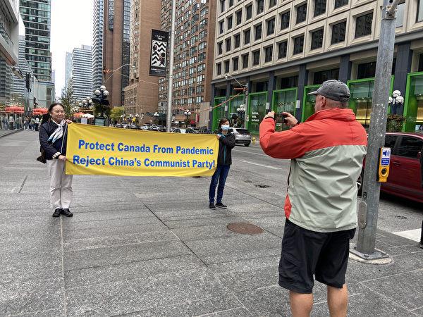 A passerby takes a photo of the volunteers holding the banner in Toronto on Oct. 10, 2020. (Dongyu Teng/The Epoch Times)