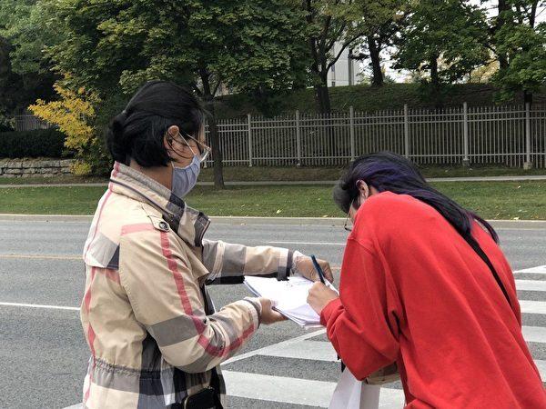 A passerby signs the petition in support of ending the CCP near Warden Avenue and Steeles in Toronto on Oct. 10, 2020. (Xuefeng Pan/Tuidang Center)