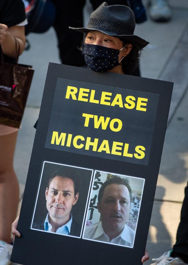 A woman holds a sign with photographs of Michael Kovrig and Michael Spavor, who have been detained in China since December, 2018, during a rally in support of Hong Kong democracy in Vancouver on Aug. 16, 2020. (The Canadian Press/Darryl Dyck)