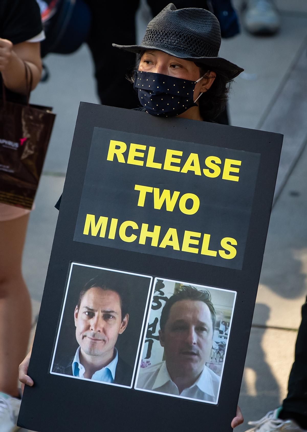 A woman holds a sign with photographs of Michael Kovrig (L) and Michael Spavor (R), who have been detained in China since December 2018, during a rally in support of Hong Kong democracy in Vancouver, Canada, on Aug. 16, 2020. (The Canadian Press/Darryl Dyck)