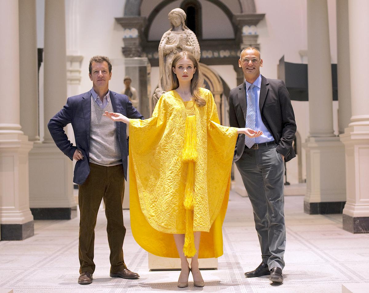 Simon Peers (L) and Nicholas Godley (R) with model Bianca Gavrilas in the hand-embroidered golden cape at The V&A Museum in London, England, on Jan. 23, 2012. (ADRIAN DENNIS/AFP via Getty Images)