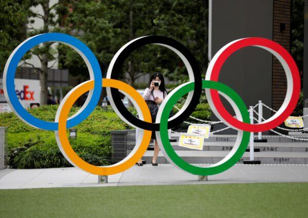 A woman wearing a protective mask takes a picture of the Olympic rings in front of the National Stadium in Tokyo, Japan, on Oct. 14, 2020. (Kim Kyung-Hoon/Reuters)