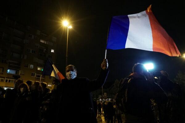 A man waves a French national flag during a silent march to pay tribute to Samuel Paty, the French teacher who was beheaded on the streets of the Paris suburb of Conflans-Sainte-Honorine, France, on Oct. 20, 2020. (Lucien Libert/Reuters)