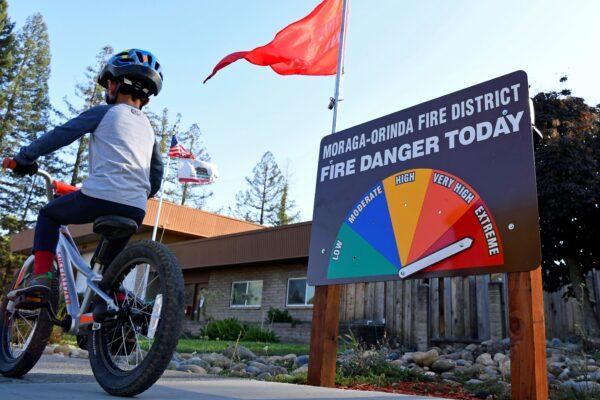 A boy rides his bike past the fire danger meter showing extreme fire danger in front of the Moraga-Orinda Fire District Station 41 in Moraga, Calif., on Oct. 25, 2020.(Jose Carlos Fajardo/Bay Area News Group via AP)