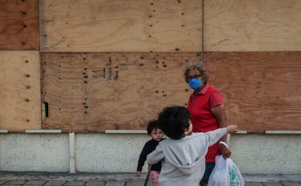 A family walks in front of a supermarket with its windows covered with plywood as Tropical Storm Zeta approaches Cancun, Mexico, on Oct. 26, 2020. (Victor Ruiz Garcia/AP Photo)