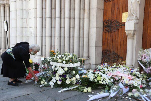 A woman, wearing a face mask, lays flowers in front of the Notre-Dame de l'Assomption Basilica during a tribute to the victims killed by a knife attacker the day before in Nice on Oct. 30, 2020. (Valery Hache/AFP via Getty Images)