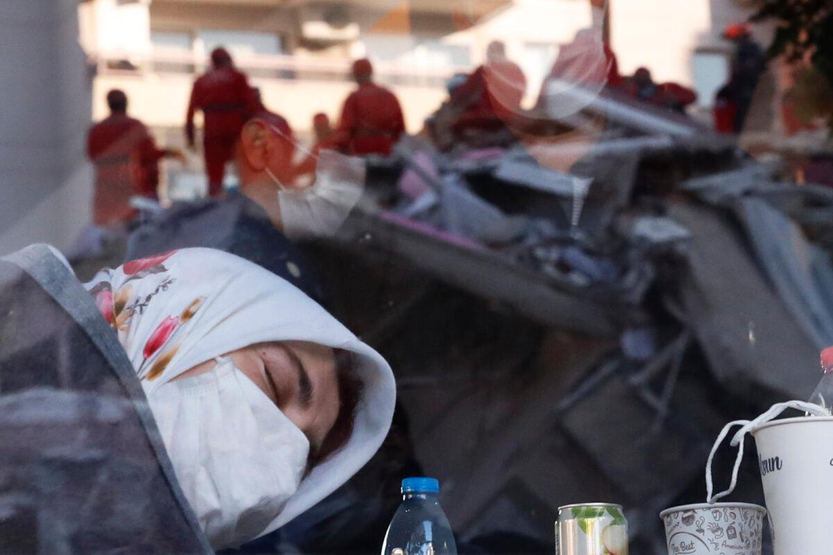 A local resident, staying outdoors for fear of aftershocks, takes a moment to relax inside a coffee shop, as members of rescue services searching for survivors in the debris of a collapsed building are reflected in the window, in Izmir, Turkey, Oct. 31, 2020. (Darko Bandic/AP Photo)