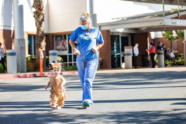 A costumed toddler and nurse hurry to join the activities at the annual Fountain Valley Regional Hospital trick-or-treat parade event in Fountain Valley, Calif., on Oct. 30, 2020. (John Fredricks/The Epoch Times)