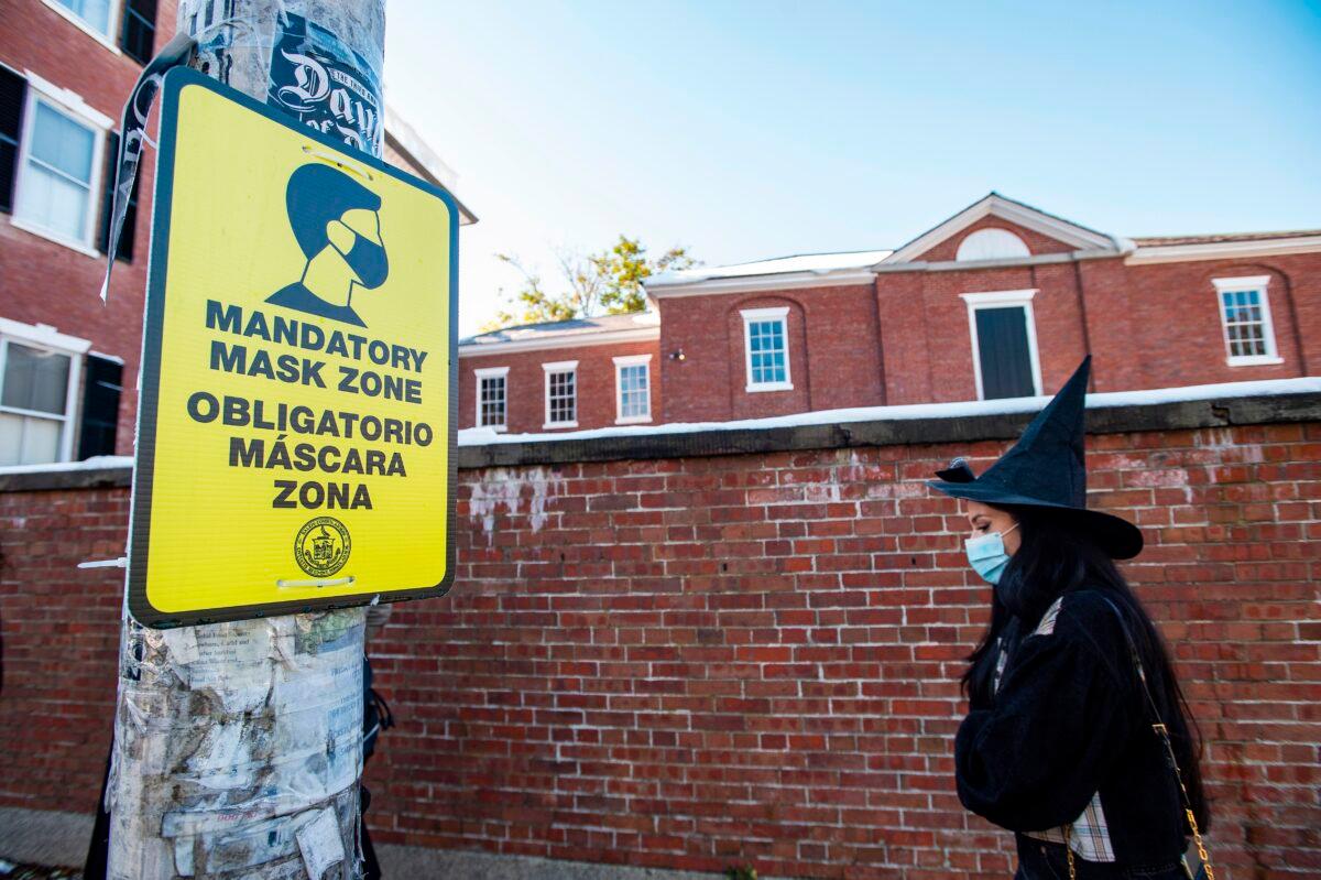 A woman dressed as a witch walks by a sign calling for mandatory mask usage on Halloween in Salem, Mass. on Oct. 31, 2020. (Joseph Prezioso/AFP via Getty Images)