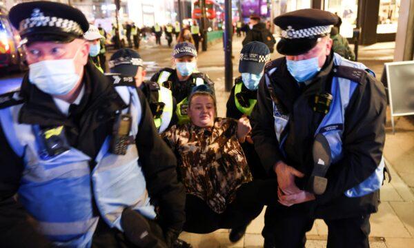 A woman is detained by police officers as protestors from the Million Mask March and anti lockdown protestors demonstrate, amid the CCP virus outbreak in London, on Nov. 5, 2020. (Henry Nicholls/Reuters)