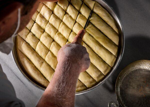  The pastry sheets are layered into a baking tray—with clarified butter brushed on each one, plus a middle layer of crushed pistachios—and the baklava is cut into pieces before baking. (Burakguralp/Shutterstock)