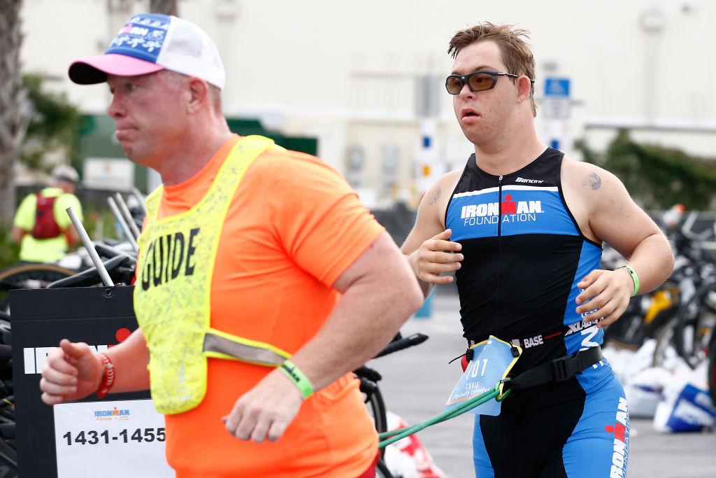 Guide Dan Grieb leads Chris Nikic through the transition from the bike portion to the run portion of IRONMAN Florida on Nov. 7, 2020, in Panama City Beach, Florida. (Michael Reaves/Getty Images)