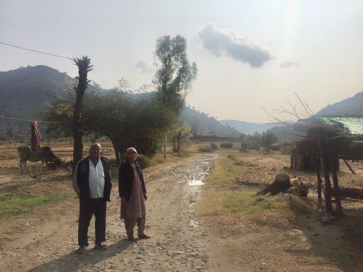 Shamsheer Singh and Billo Devi stand outside their home. The disputed India–Pakistan border can be seen behind them. (Venus Upadhayaya/Epoch Times)